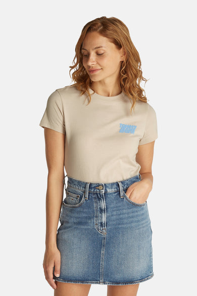 T-shirt écru à manches courtes de Tommy Jeans, avec logo bleu sur le devant, porté avec une jupe en jean.
