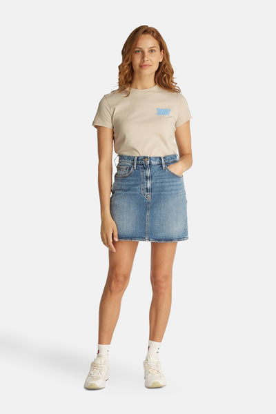 T-shirt écru à manches courtes de Tommy Jeans, porté avec une jupe en jean bleu et des baskets blanches.