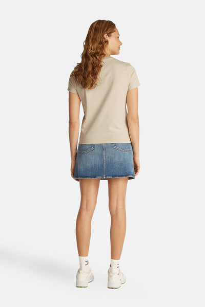 Top uni manches courtes écru de Tommy Jeans avec une jupe en jean bleu et des chaussures blanches.

