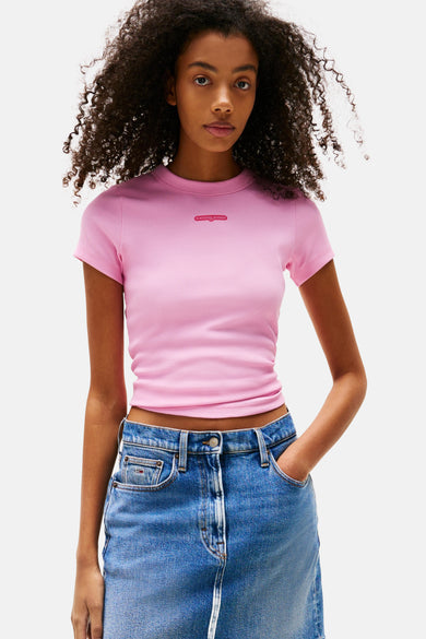 Roze T-shirt met korte mouwen van TOMMY JEANS, gedragen met een korte spijkerrok en witte sneakers.