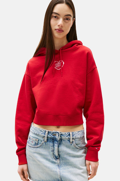 Rode TOMMY JEANS sweater, kort, met capuchon en geborduurd logo op de voorkant, gedragen met een low-rise jeans.