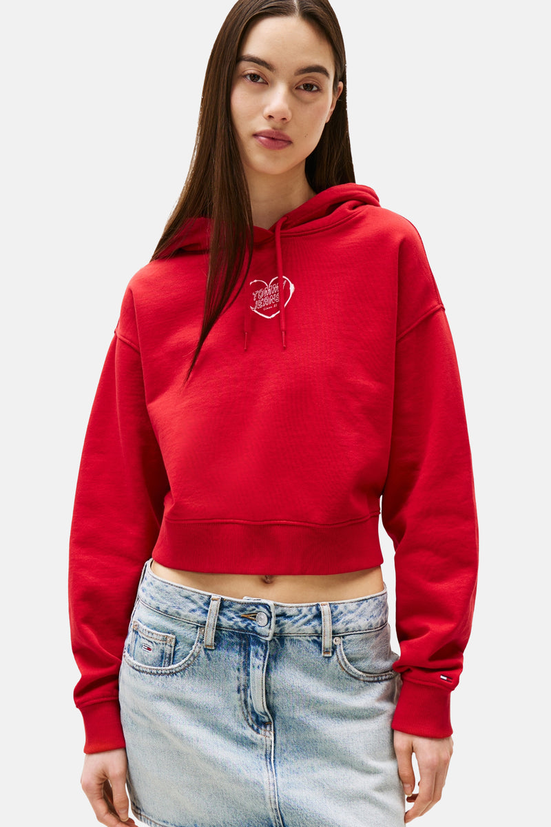 Rode TOMMY JEANS sweater, kort, met capuchon en geborduurd logo op de voorkant, gedragen met een low-rise jeans.