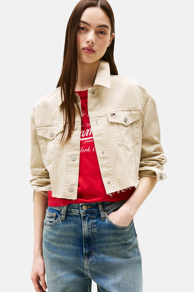 Korte beige jas van TOMMY JEANS met metalen knopen, gedragen over een rood T-shirt en een blauwe jeans.