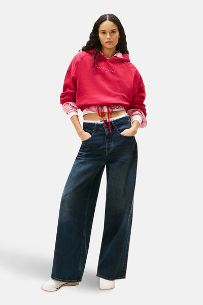 Roze hoodie van Tommy Jeans, gedragen met een gestreept overhemd en een high-waisted jeans.