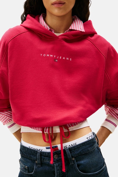 Roze hoodie van Tommy Jeans, gedragen met een gestreept overhemd en een low-rise jeans.