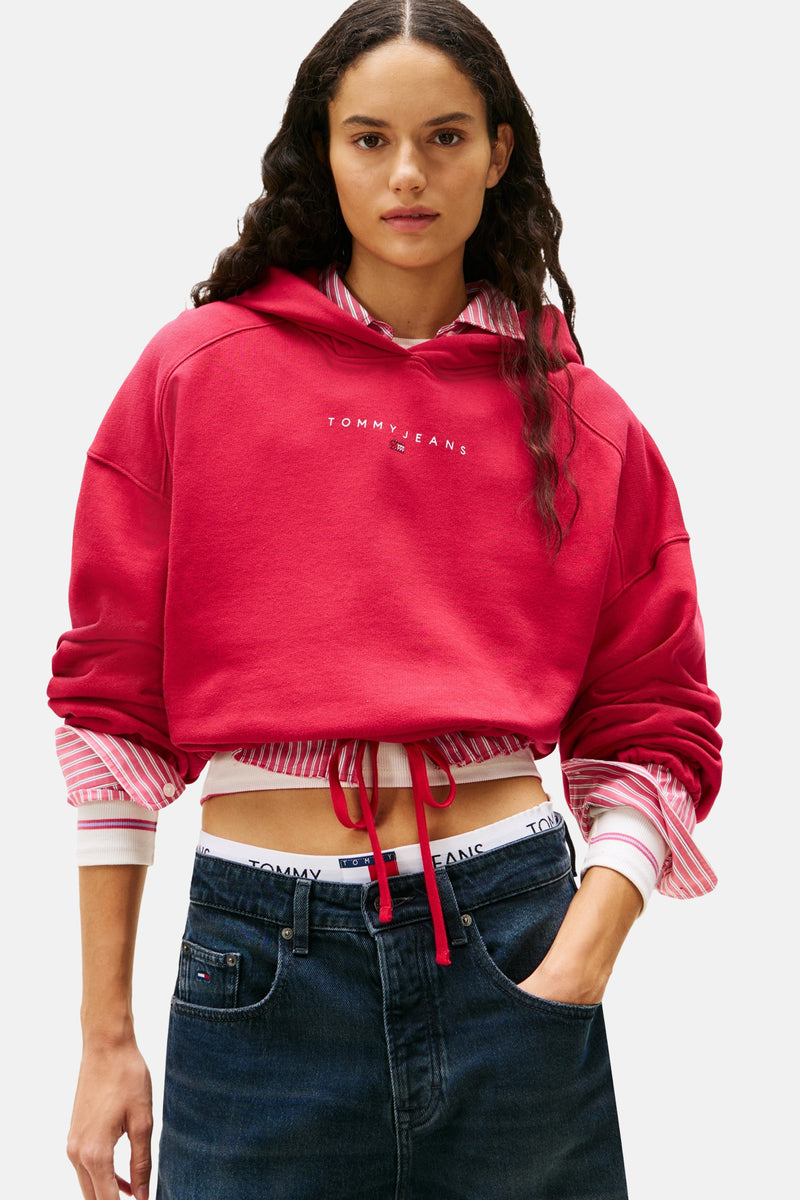 Roze hoodie van TOMMY JEANS, gedragen over een gestreept overhemd en een low-rise jeans.