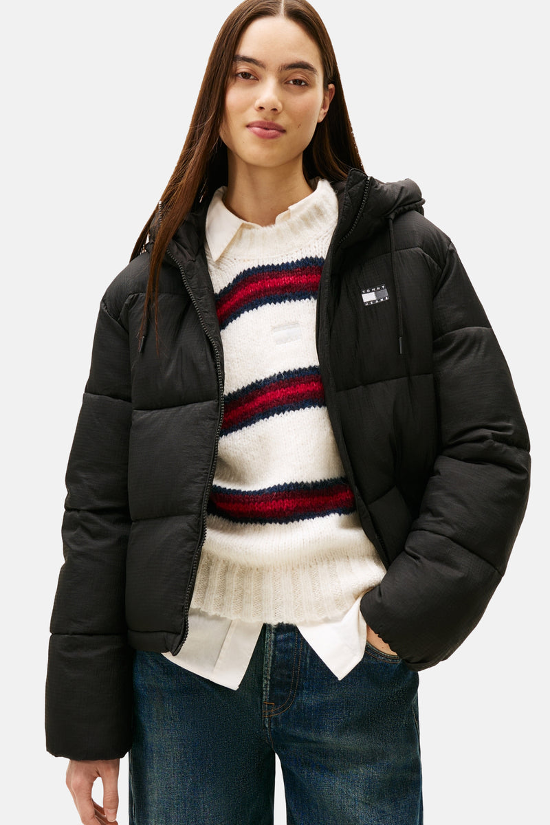 Veste courte noire de TOMMY JEANS, portée sur un pull rayé et un chemisier blanc, avec un jean.
