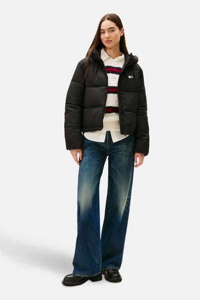 Veste courte noire par TOMMY JEANS, portée avec un pull rayé et un jean ample.