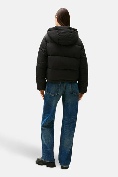 Veste courte noire de Tommy Jeans, avec capuche, portée avec un jean bleu ample et des chaussures noires à plateforme.