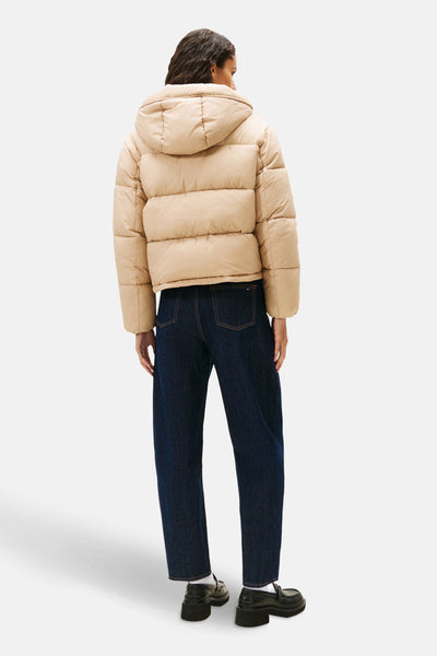 Korte beige jas van TOMMY JEANS, met capuchon, gedragen met een donkerblauwe jeans en zwarte loafers.