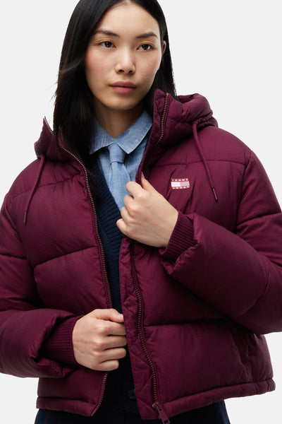 Femme portant une veste matelassée bordeaux TOMMY JEANS à capuche, avec logo visible.