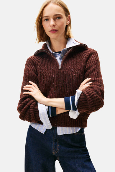Bruine trui met dikke kabelsteek van TOMMY JEANS, gedragen over een gestreept overhemd en een donkere spijkerbroek.