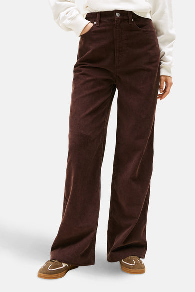 Pantalon brun en velours côtelé de Tommy Jeans, porté avec un pull blanc et des baskets marron.