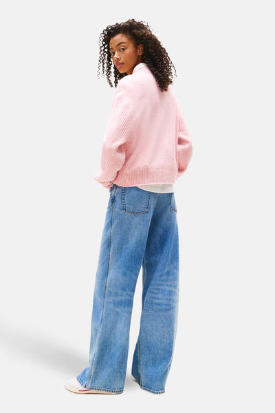 Pull à col rond rose de TOMMY JEANS, porté avec un jean ample bleu et des baskets blanches, vue de dos.