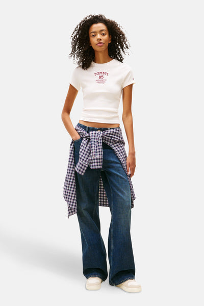 T-shirt blanc à manches courtes de TOMMY JEANS, porté avec une chemise à carreaux nouée et un jean ample.