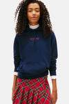 Blauwe hoodie van TOMMY JEANS met rood logo, gedragen met een geruite rok, witte sokken en sneakers.