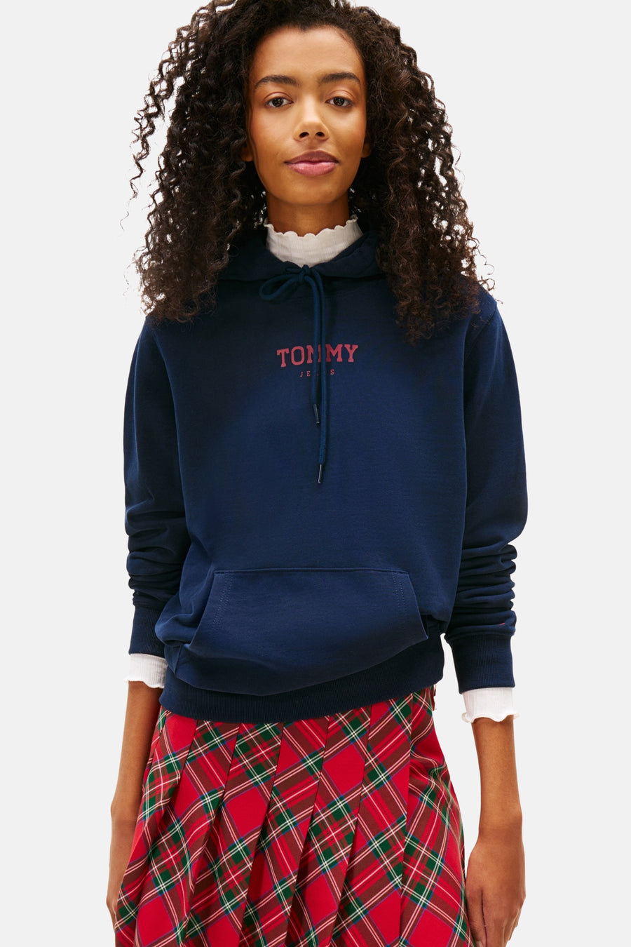 Blauwe hoodie van TOMMY JEANS met rood logo, gedragen met een geruite rok, witte sokken en sneakers.