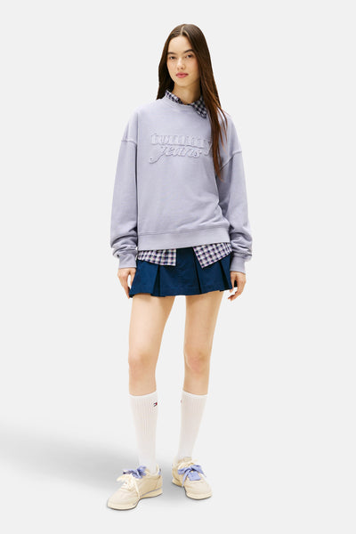 Mauve rondehals sweatshirt van TOMMY JEANS, gedragen over een geruit overhemd en een geplooide rok, met sokken en sneakers.