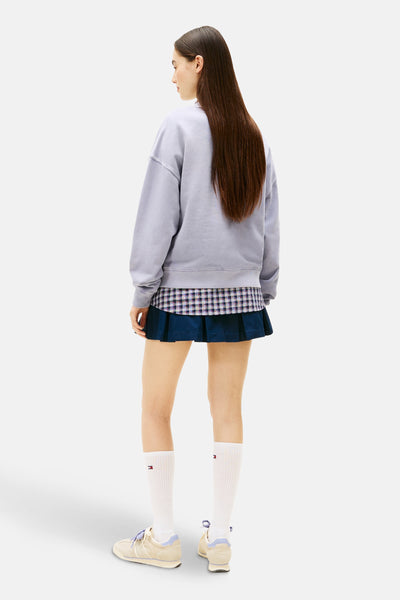 Sweat mauve de TOMMY JEANS, porté avec une chemise à carreaux et une jupe plissée marine.