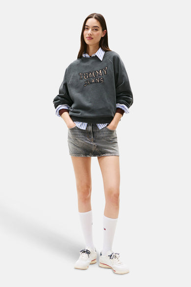 Grijze sweater van TOMMY JEANS, gedragen over een blauw gestreept overhemd, met een spijker-minirok en hoge witte sokken.