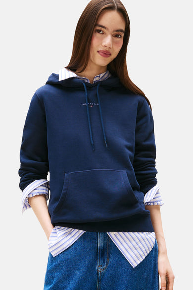 Marineblauwe hoodie van TOMMY JEANS, gedragen over een gestreept overhemd en een blauwe jeans
