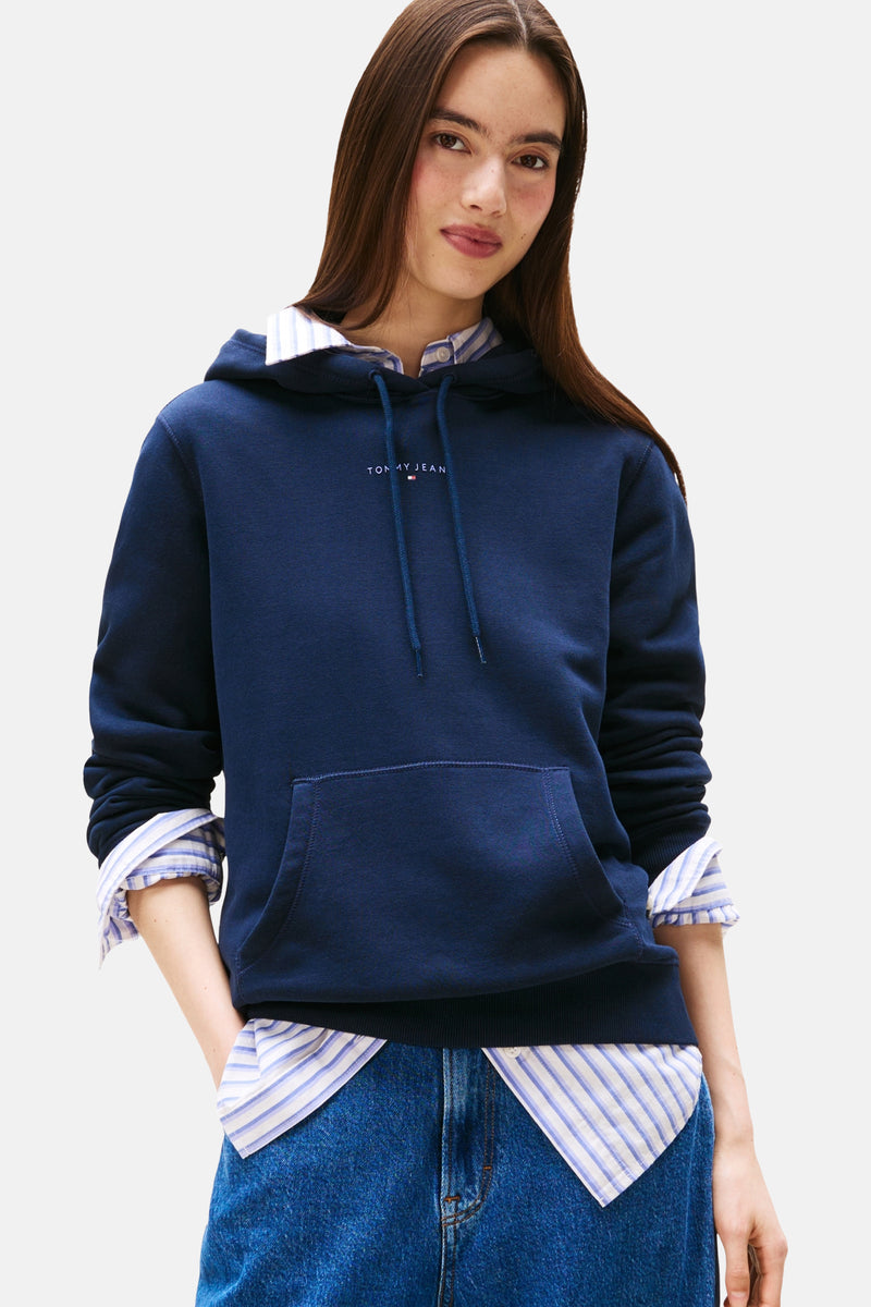 Marineblauwe hoodie van TOMMY JEANS, gedragen over een gestreept overhemd en een blauwe jeans
