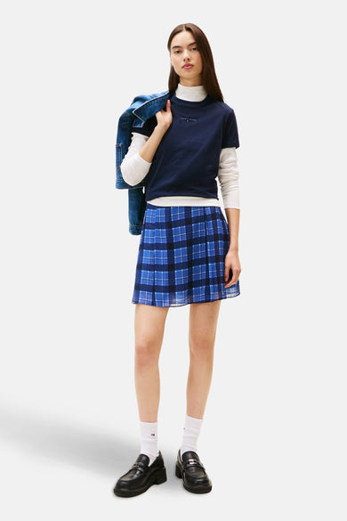 Blauw T-shirt met korte mouwen van TOMMY JEANS, gedragen over een witte coltrui, met een blauw-zwarte Schotse rok.