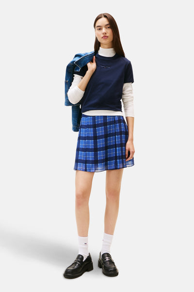 Blauw T-shirt met korte mouwen van TOMMY JEANS, gedragen over een witte coltrui, met een blauw-zwarte Schotse rok.