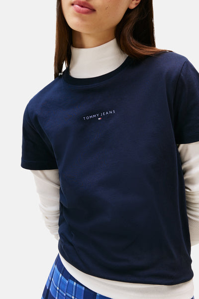 Blauwe T-shirt met korte mouwen van Tommy Jeans, gedragen over een witte geribbelde coltrui, met discreet logo.