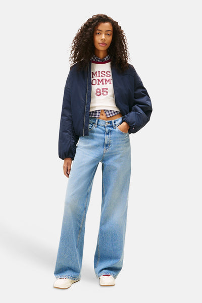 Jean large bleu moyen en denim de Tommy Jeans, porté avec un t-shirt et une veste bomber.
