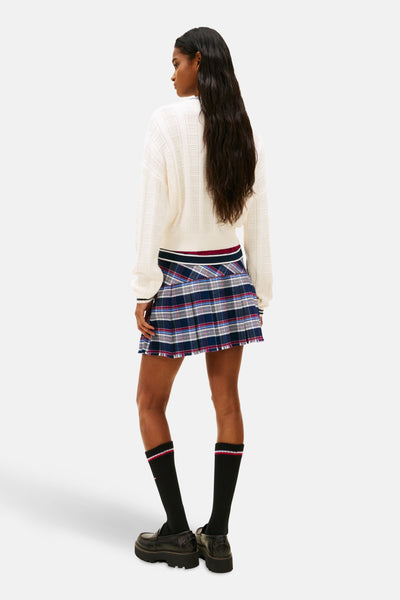 Pull à col rond blanc de TOMMY JEANS, motif géométrique, porté avec une jupe écossaise et des chaussettes montantes.