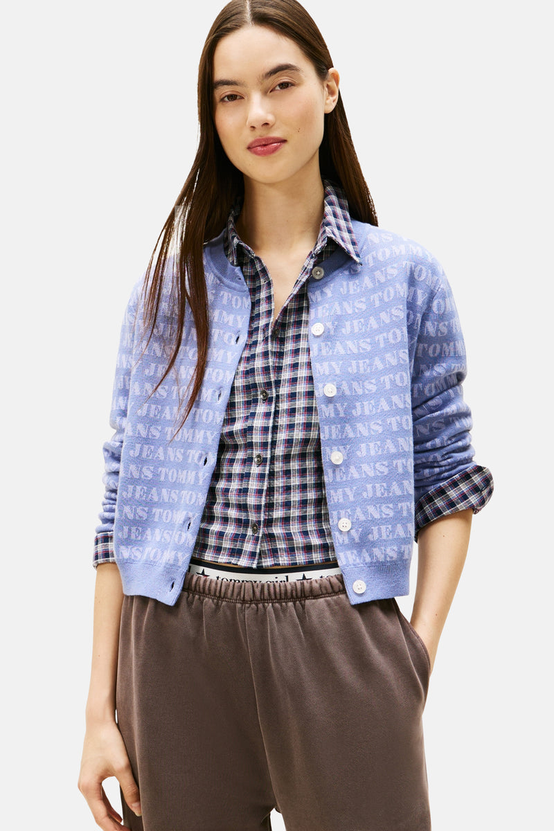 Cardigan mauve en tricot, de TOMMY JEANS, avec un motif à lettres sur l'ensemble et porté sur une chemise à carreaux.
