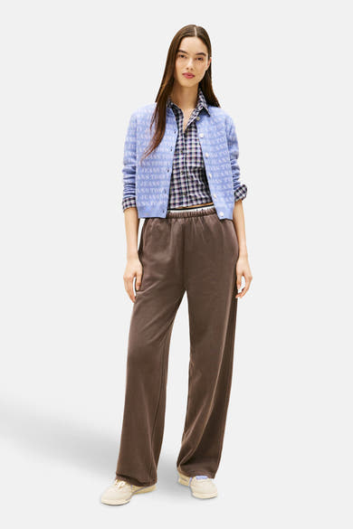 Mauve cardigan bedrukt met logo's van TOMMY JEANS, gedragen over een geruit overhemd met een bruine broek.