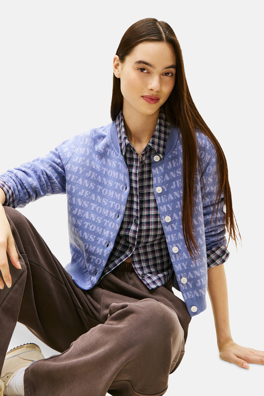 Mauve cardigan van TOMMY JEANS, met all-over logoprint, gedragen over een geruit overhemd en een bruine broek.