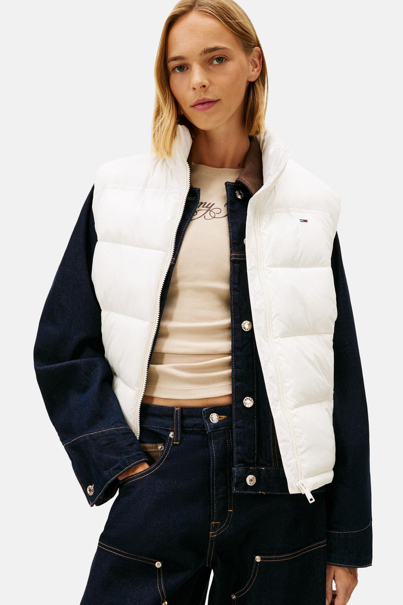 Witte mouwloze jas van TOMMY JEANS, gedragen met een spijkerjas en een donkere broek, van achteren gezien.