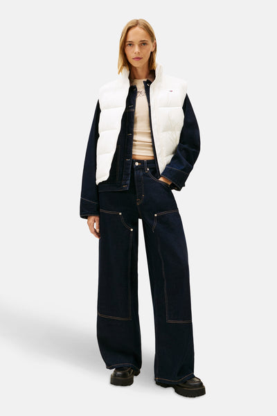 Witte mouwloze jas van Tommy Jeans, gedragen over een oversized spijkerjas en een marineblauwe broek.