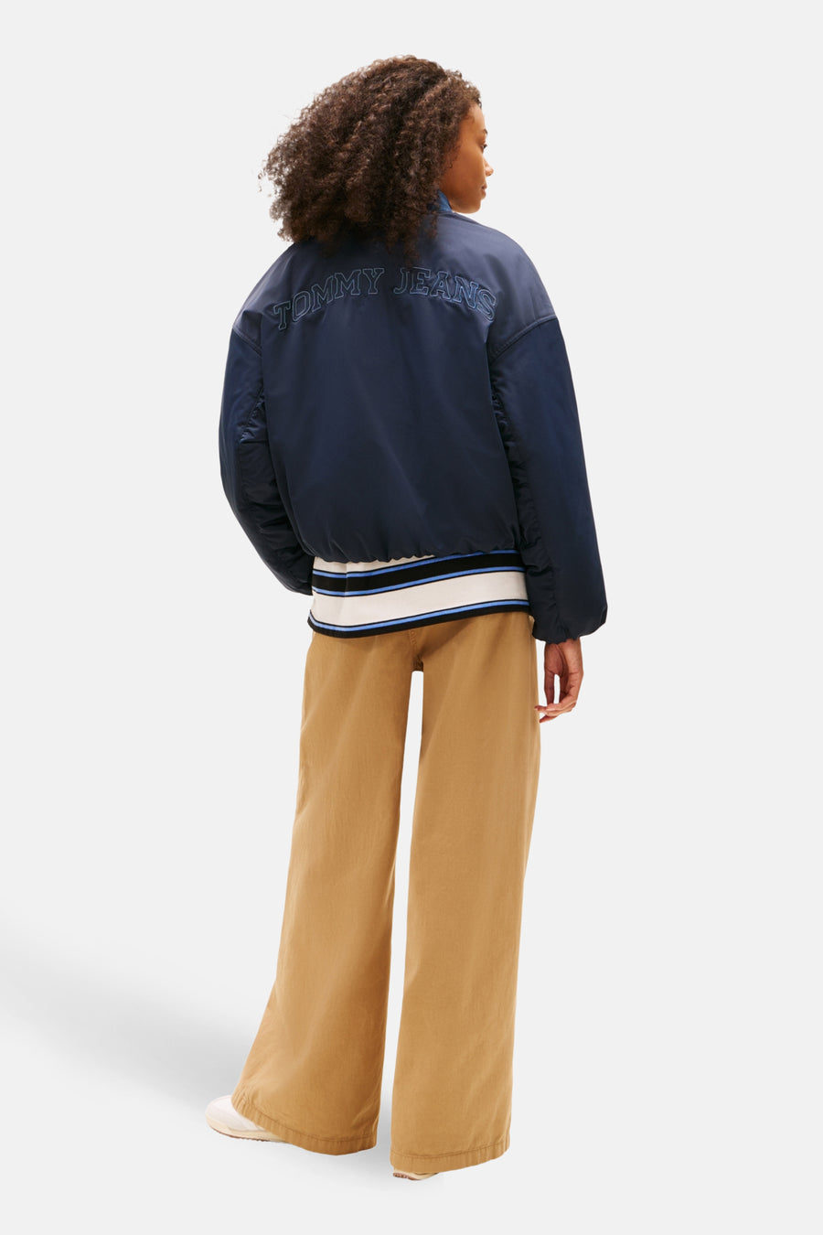 Veste courte bleue de TOMMY JEANS avec inscription au dos, portée avec un pantalon beige