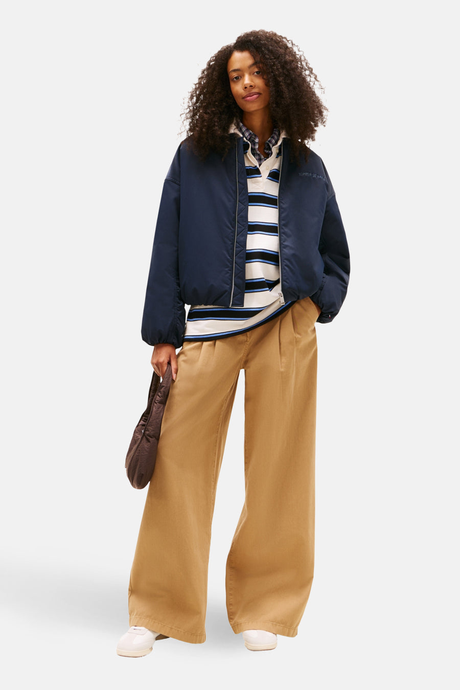 Veste courte bleue de TOMMY JEANS avec un pull rayé, un pantalon beige ample et un sac marron.