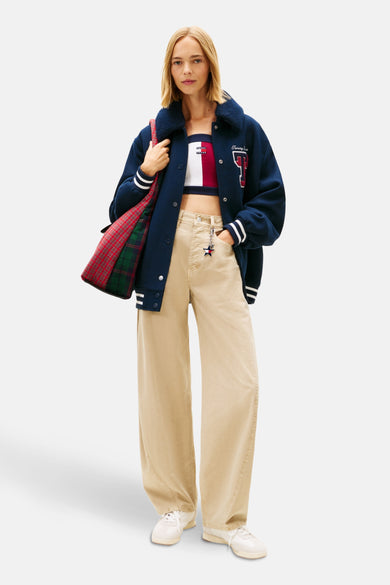 Beige broek van TOMMY JEANS, wijde pasvorm, gedragen met een gestreept topje en een marineblauwe varsity jas.
