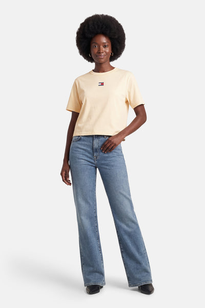 T-shirt jaune à manches courtes de TOMMY JEANS, porté avec un jean bleu taille haute et des bottes noires.