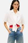 Chemise blanche à manches courtes de TOMMY JEANS, nouée devant avec un débardeur rouge et un jean taille haute.
