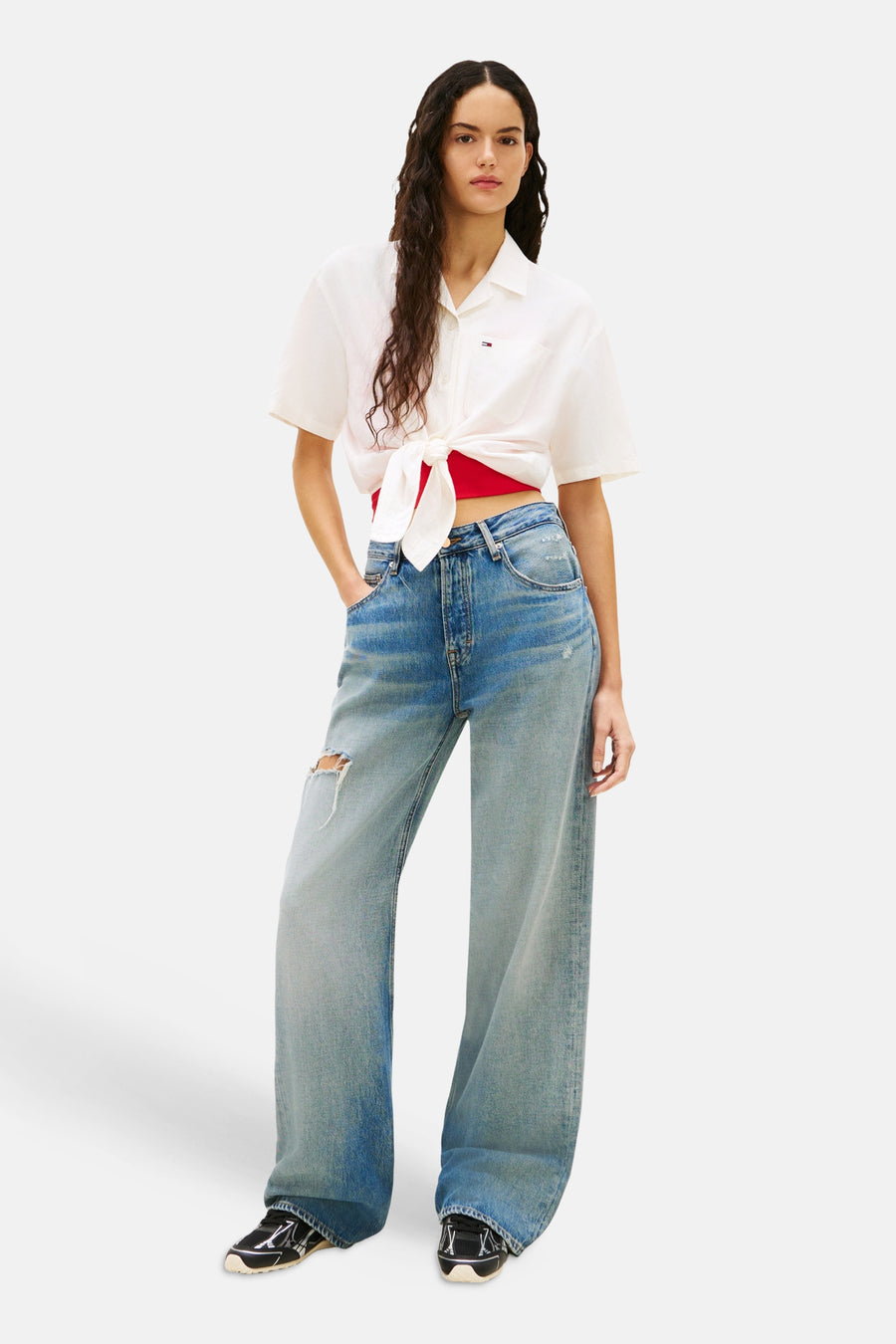 Chemisier blanc à manches courtes de TOMMY JEANS noué sur un top rouge, porté avec un jean ample bleu délavé