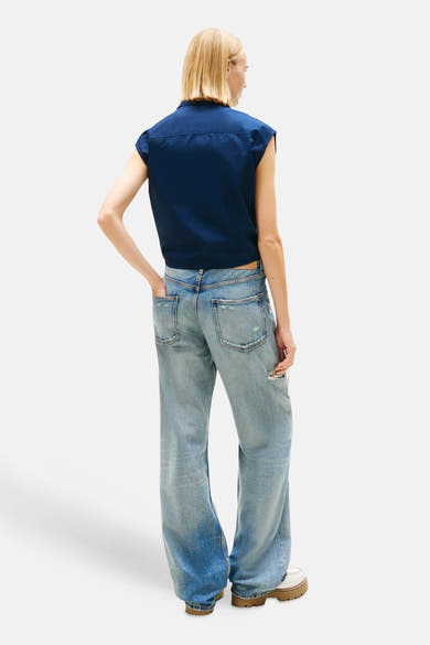 Blauwe blouse van TOMMY JEANS, mouwloos model, gedragen met een wijde, uitgewassen spijkerbroek en schoenen met dikke zool.
