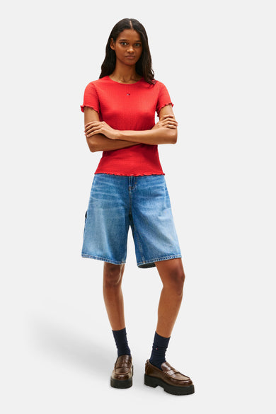 T-shirt rouge à manches courtes de Tommy Jeans, avec un ourlet ondulé, porté avec un short en jean ample.