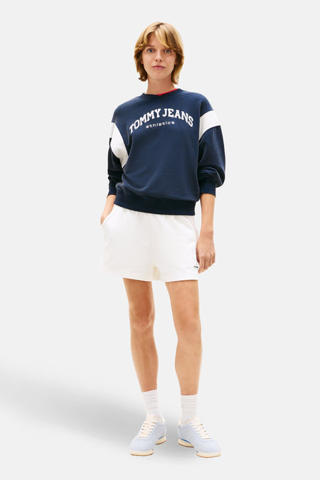 Short blanc de Tommy Jeans, porté avec un pull bleu marine à logo, des chaussettes blanches et des baskets bleues.
