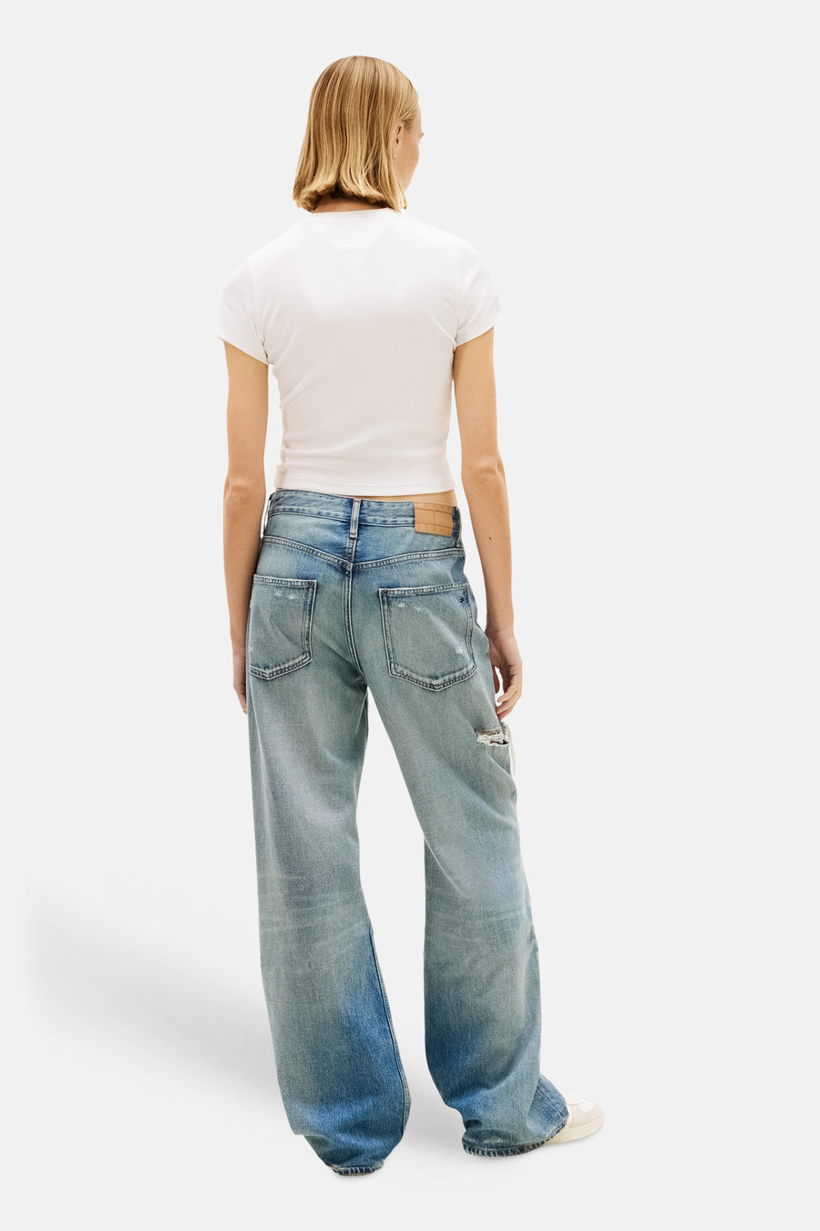 Wit T-shirt van TOMMY JEANS, gedragen met een wijde, uitgewassen en gescheurde spijkerbroek, achtergezicht.
