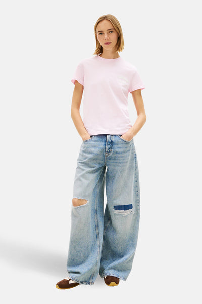 T-shirt rose à manches courtes de TOMMY JEANS, avec un logo blanc sur la poitrine, porté avec un jean ample déchiré.