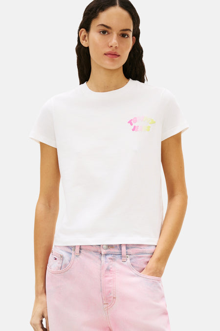T-shirt blanc à manches courtes de Tommy Jeans, avec un logo coloré sur le devant, porté avec un jean rose.
