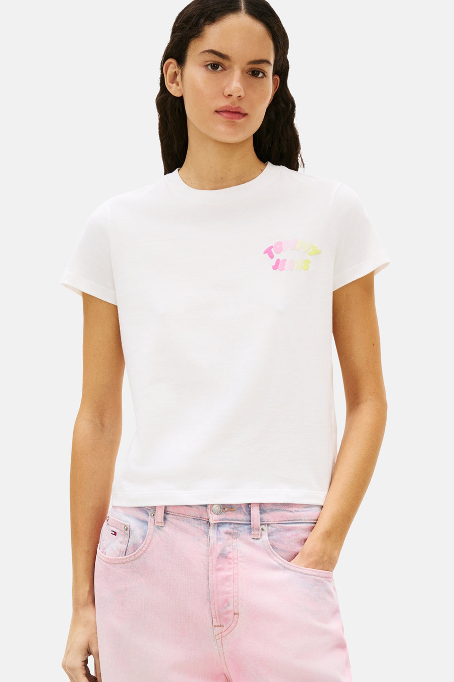 Wit T-shirt met korte mouwen van Tommy Jeans, met een logo op de voorkant, gedragen met een roze broek met hoge taille.