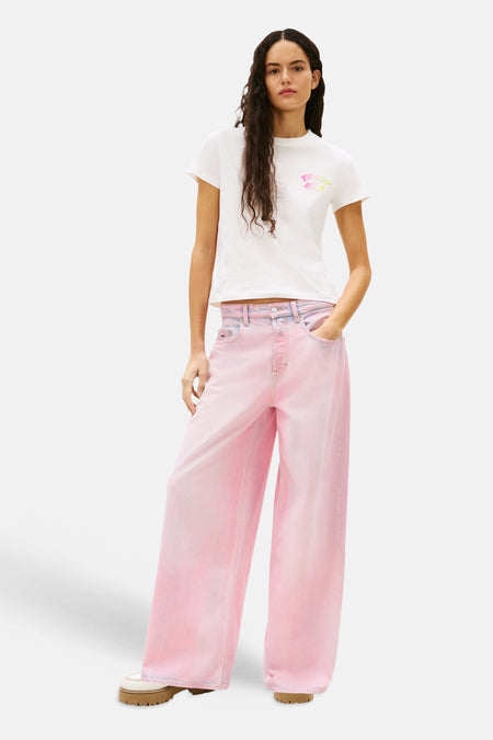 T-shirt à manches courtes blanc de Tommy Jeans, avec un logo sur le devant, porté avec un pantalon rose taille haute.